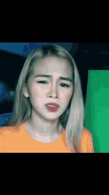 a woman with blonde hair is wearing an orange shirt and making a funny face .
