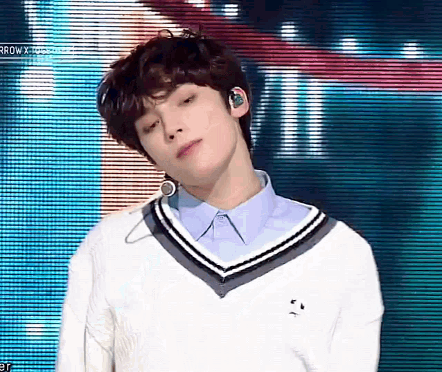 a young man wearing a white sweater and a blue shirt is standing in front of a screen .