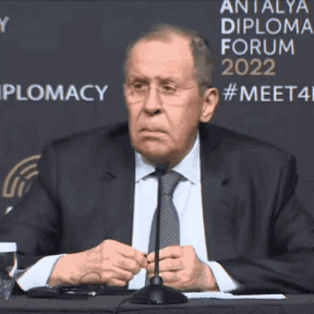 a man in a suit and tie is sitting in front of a sign that says diplomacy 2022
