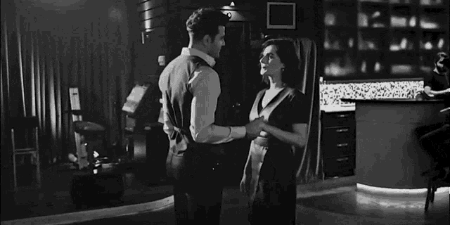 a black and white photo of a man and woman hugging each other in a bar .