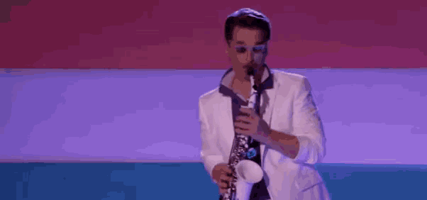 a man in a white suit is playing a saxophone on a stage in front of a pink and blue background .