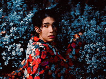 a man in a floral shirt is standing in a field of flowers