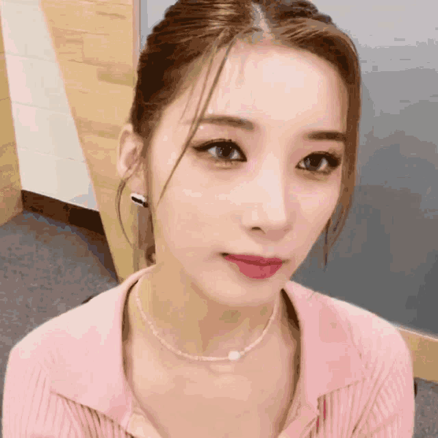 a close up of a woman wearing a pink shirt and pearl necklace