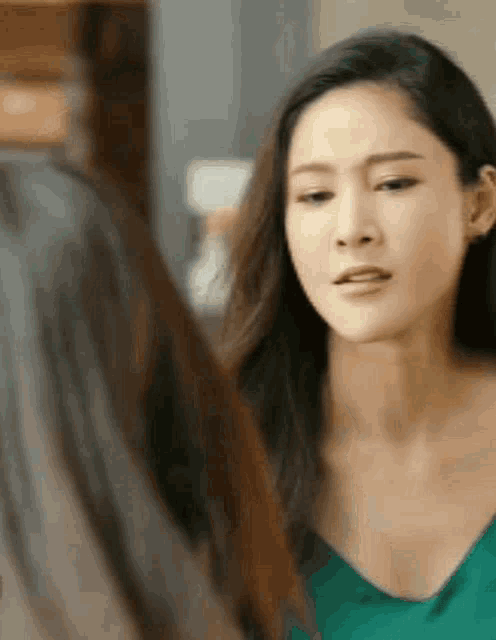 a woman in a green top is looking at herself in the mirror .