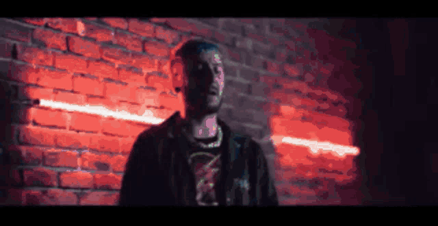 a man stands in front of a brick wall with red lights behind him