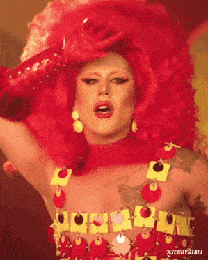 a drag queen is wearing a red wig and a red and yellow dress