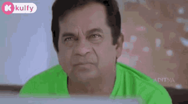 a man in a green shirt is making a funny face with his hand on his mouth .
