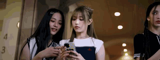 three girls are standing next to each other looking at a cell phone