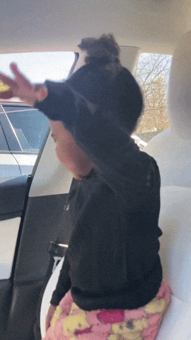 a child sitting in the back seat of a car with her arms outstretched
