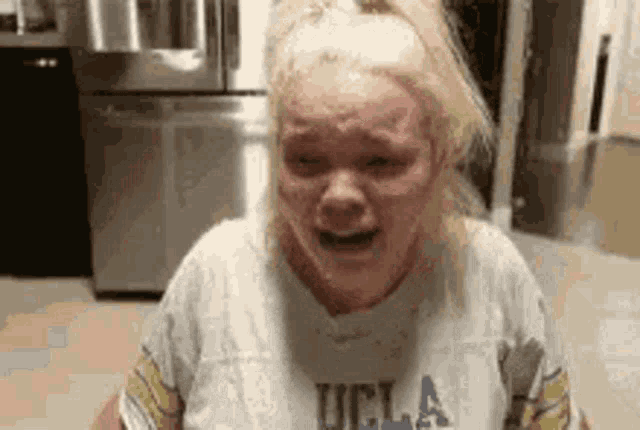 a woman wearing a ucla t-shirt is crying in a kitchen .