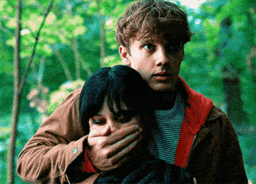 a man covering a woman 's mouth with his hand in a forest