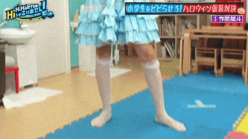 a girl in a blue dress and white socks is standing on a blue mat with a sign that says hi-hello