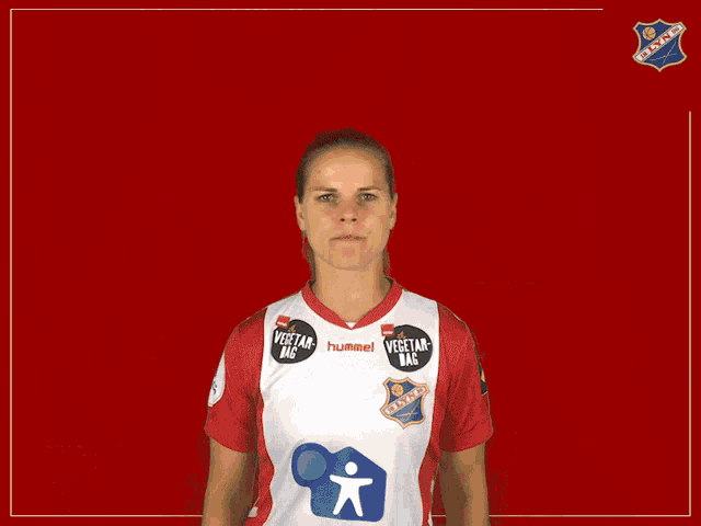 a woman wearing a red and white hummel shirt is making a face