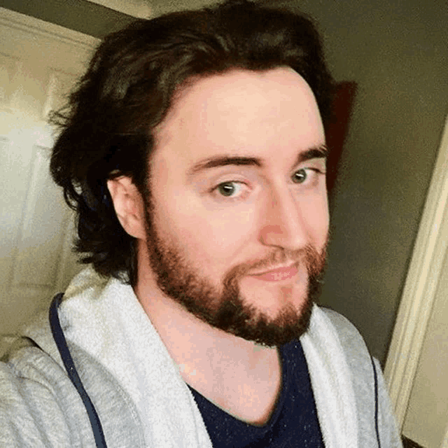 a man with long hair and a beard is wearing a gray sweatshirt