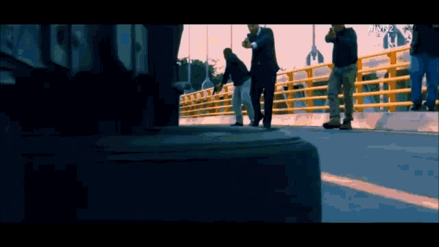 a group of men are walking across a bridge and one of them has a gun in his hand