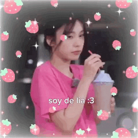 a girl in a pink shirt is drinking from a cup with strawberries .