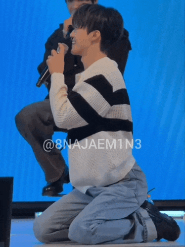 a young man kneeling down with a microphone in his hand and the hashtag @ 8najaem1n3