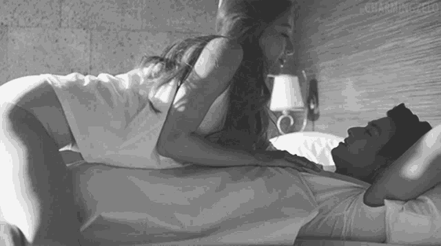 a black and white photo of a woman kissing a man in bed