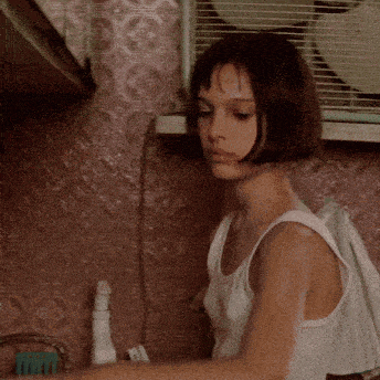 a girl in a white tank top is standing in front of a fan