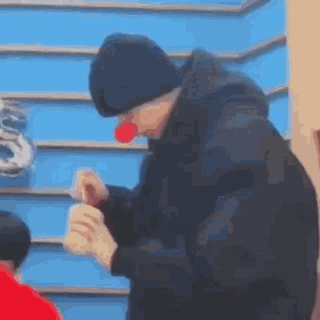 a man wearing a clown nose and a black jacket is eating a sandwich .