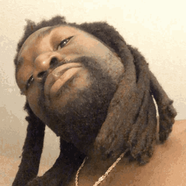 a man with dreadlocks and a gold chain around his neck looks up at the camera