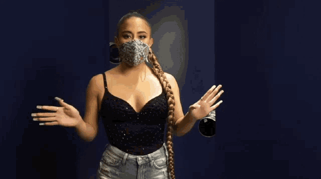 a woman wearing a black top and denim shorts is wearing a face mask