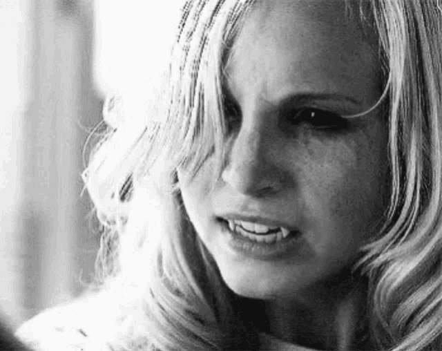 a black and white photo of a woman with vampire teeth looking at the camera .