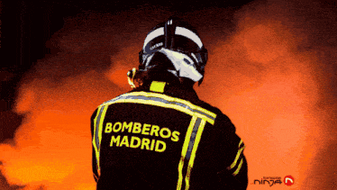 a fireman in a bomberos madrid uniform stands in front of a fire