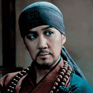 a man with a beard wears a headband and a necklace of beads