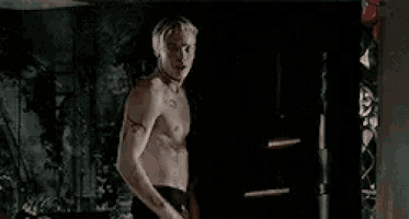 a shirtless man is standing in a dark room holding his hair .