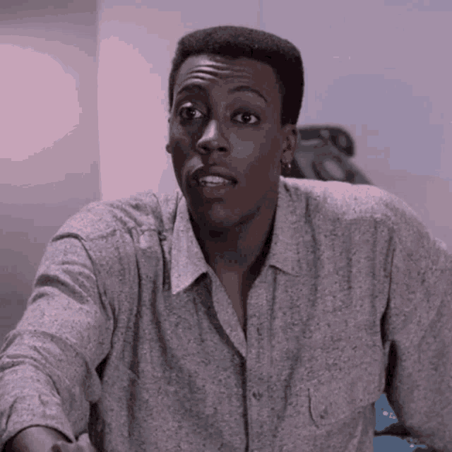 a man wearing a grey shirt and earrings is looking at the camera