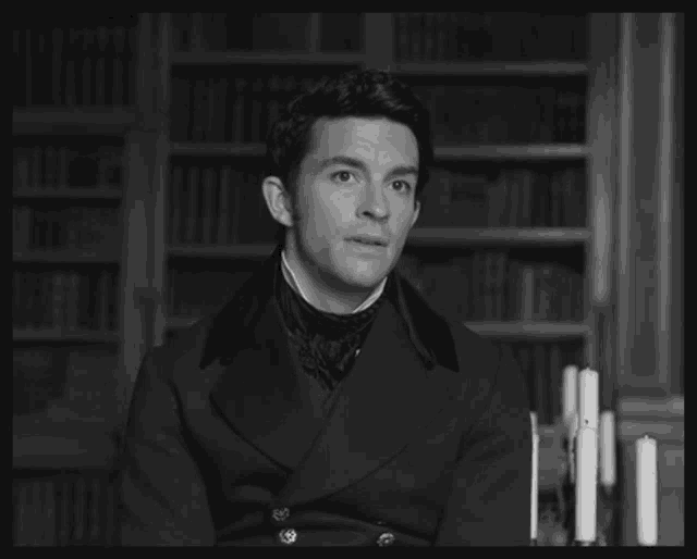 a black and white photo of a man sitting in front of a bookshelf