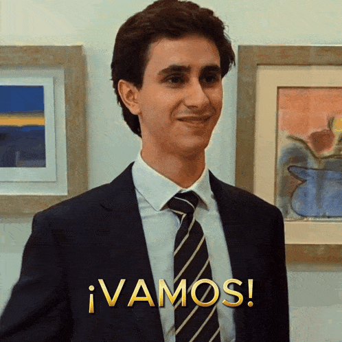 a man in a suit and tie is standing in front of a framed painting and says vamos