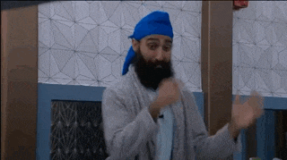 a man with a beard and a blue turban is standing in a room with his arms outstretched .