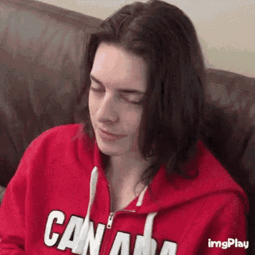 a woman is sitting on a couch wearing a red canada sweatshirt .