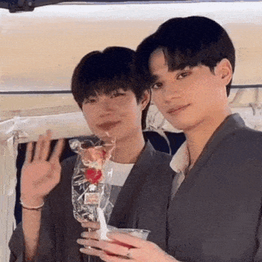 a couple of young men are standing next to each other and waving at the camera .