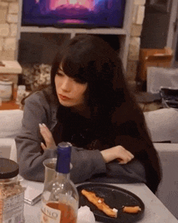 a woman is sitting at a table with a plate of food , a bottle of wine , and a television .