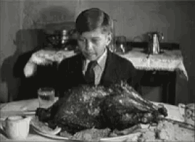 a boy in a suit and tie is sitting at a table with a turkey on it .