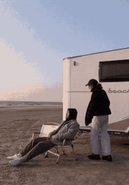 a man sits in a chair on the beach next to a camper that says beach