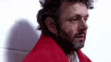 a man with a beard is wrapped in a red blanket against a white wall