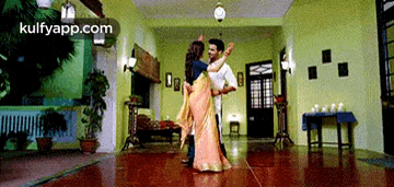 a man and a woman are dancing in a living room and the website kulfyapp.com is visible in the corner