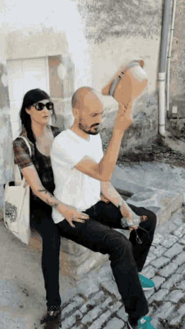 a man and a woman are sitting on a stone ledge and the man is holding a hat