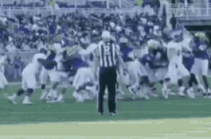 a referee is standing in the middle of a football game with players fighting on the field .