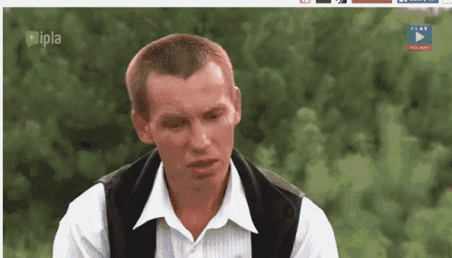a man in a white shirt and black vest is sitting in front of trees .