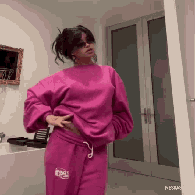 a woman in a pink sweatshirt and sweatpants is standing in front of a door