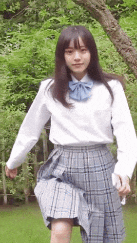 a girl wearing a white shirt and a blue bow tie is standing in front of a tree .