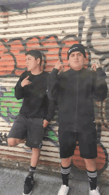 two boys standing in front of a graffiti covered wall