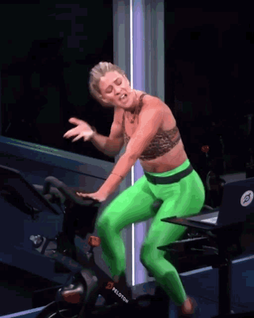 a woman in green pants is riding a peloton exercise bike