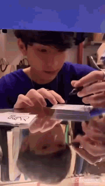 a young man is writing on a piece of paper with a pen while sitting at a table .