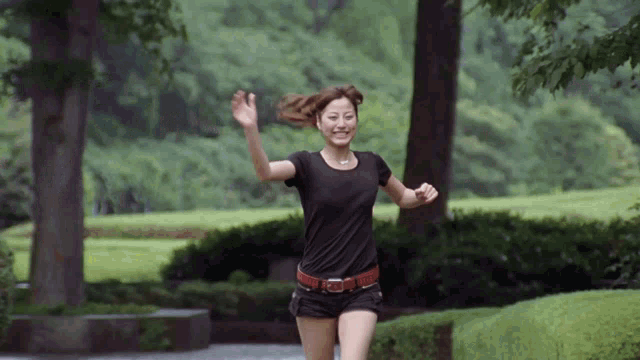 a woman wearing a black shirt and shorts is running in a park